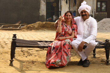 Aged man sitting in Rural Environment wearing kurta-pajama which is traditional Dress for men in North India in day time with his wife.