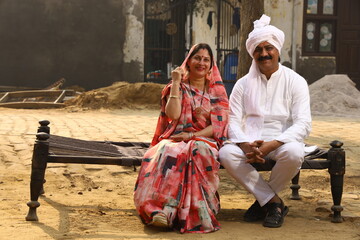 Aged man sitting in Rural Environment wearing kurta-pajama which is traditional Dress for men in North India in day time with his wife.