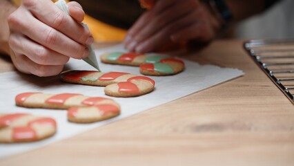 Using delicate lines, the woman is piping green icing onto the gingerbread cookie and filling it in, in a close-up view.