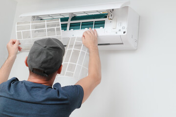 Air conditioner service indoors. Male Technician removing air filter of the air conditioner for cleaning.