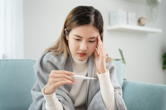 Young Asian woman having high fever while checking body temperature, female sneezing and runny nose with seasonal influenza, allergic, digital thermometer, virus, coronavirus, illness, respiratory.