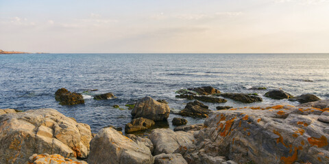 Fototapeta na wymiar seashore with rocks at sunrise. bright morning sky above horizon. sunny weather