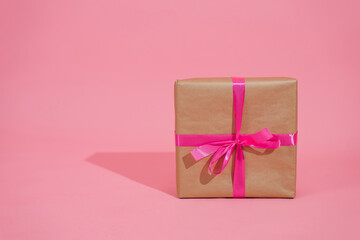 Gift box on pink background. A gift in gold paper, decorated with a stylish elegant fuchsia satin ribbon bow. The concept of Christmas and any other holidays