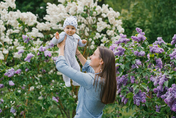 Obraz premium Happy European mother lifts up her little smiling son in her arms in the spring on a walk in the park