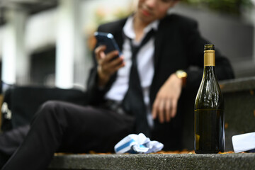 A bottle of alcohol on stairs with desperate businessman. Lost, unemployed, alcoholism problem or bankrupt
