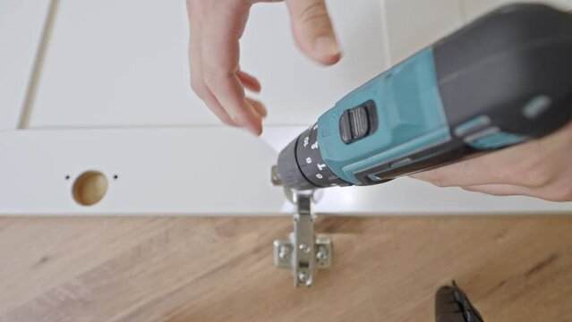Screwing closet door hinges in place with power drill, top down view