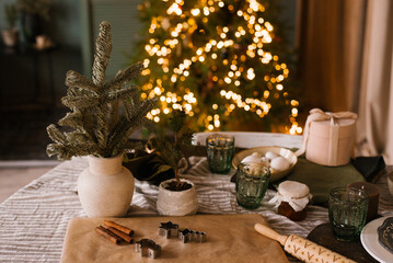 Christmas decor on the background of lights. Christmas tree branches in a vase, rolling pin, ginger...
