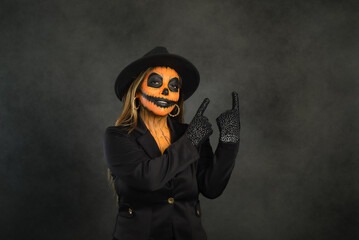 Woman in pumpkin makeup to celebrate Halloween pointing to a blank space.