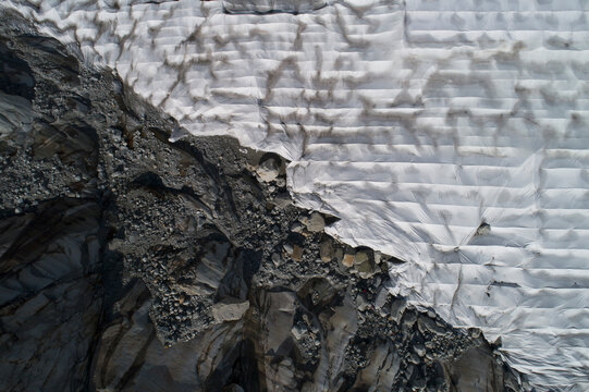 Aerial view textured rocks and protective tarpaulin over Rhone Glacier, Switzerland
