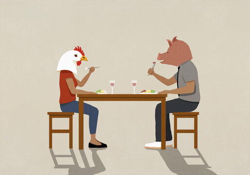 Couple wearing pig and chicken heads eating dinner at dining table
