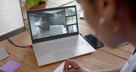 African american female security officer watching business cctv camera views on laptop, slow motion - Powered by Adobe