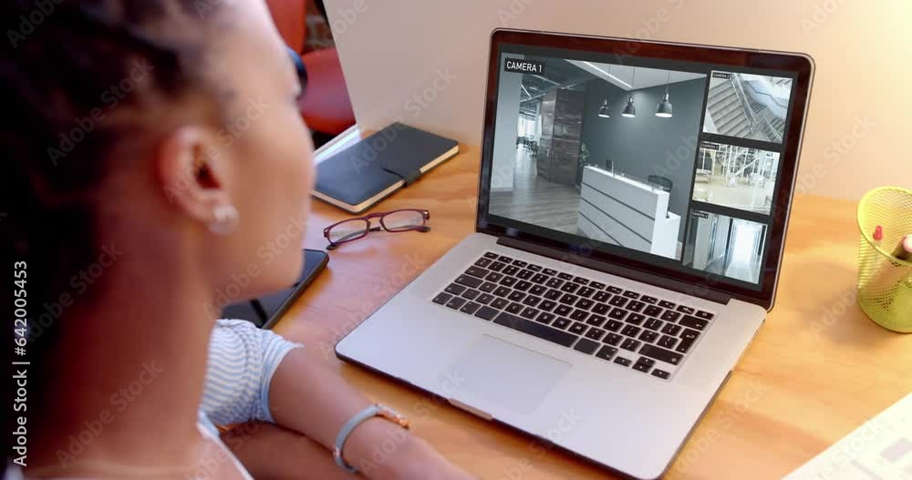 Poster African american female security officer watching business cctv camera views on laptop, slow motion