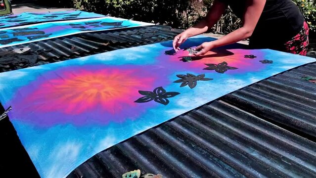 Using stencils onto a tie dye fabric to bleach patterns into the colour