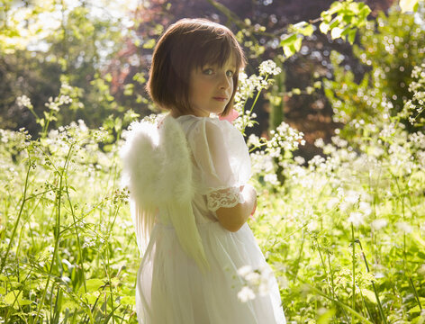 Portrait of young girl in a white fairy costume standing in a garden
