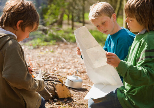 Three boys kneeling around campfire looking at map
