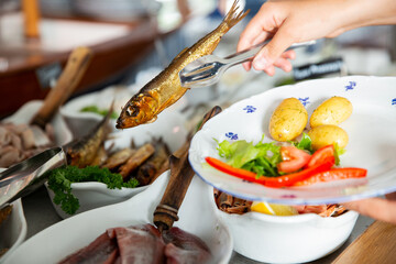 A restaurant customer puts delicious smoked Baltic herring on a plate. Seafood buffet lunch in a...