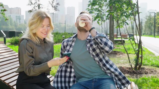 A young blonde woman and a handsome man are sitting on a park bench and talking