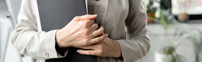 cropped view of mature entrepreneur holding folders with documents in contemporary office, banner