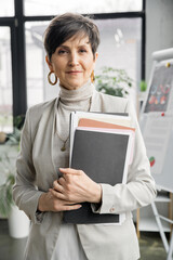 confident mature businesswoman looking at camera in office, folders, documents, portrait, headshot