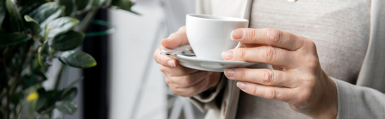 cropped view of middle aged entrepreneur with coffee cup standing in office, banner