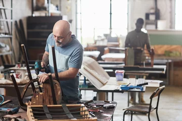 Gardinen Portrait of senior craftsman in furniture restoration workshop fixing old wooden chair, copy space © Seventyfour