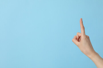 Female hand showing index finger on blue background, place for text