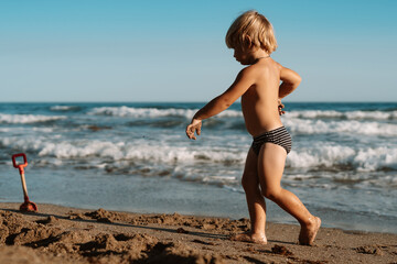 Fototapeta na wymiar little boy 3 years old plays in the sand on the beach near the sea