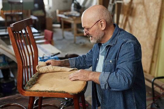 Side view portrait of senior man in furniture restoration workshop fixing old chair