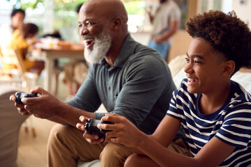 Fototapeta premium Grandfather And Grandson Sitting On Sofa At Home Playing Video Game Together