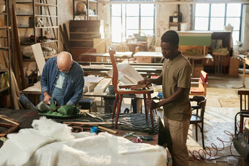 Portrait of two people working on furniture restoration in workshop lit by sunlight, copy space