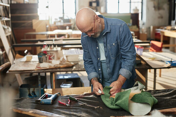 Waist up portrait of senior craftsman refurbishing vintage furniture in rustic workshop, copy space