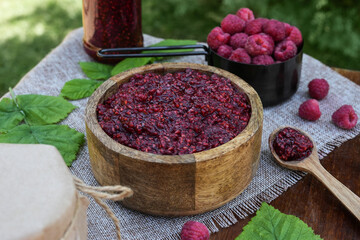 Raspberry jam with berry in wooden bowl on dark background. Homemade jam with raspberry. Banner, menu, recipe. Side view, place for text.