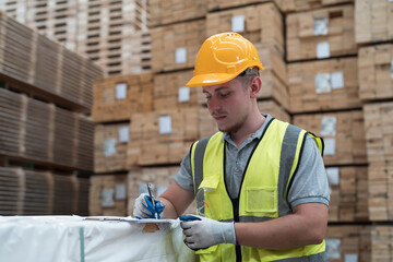 Male warehouse worker wearing uniform checks stock inventory in wooden warehouse storage. Male worker working in wooden warehouse - obrazy, fototapety, plakaty