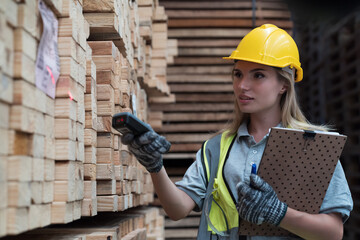 Female warehouse worker scanning barcodes on pile of plank wooden in wooden warehouse storage. Woman worker working in wood warehouse storage
