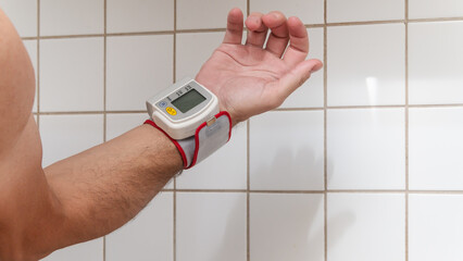 Small modern blood pressure measuring device is fit to a man hand at home bathroom.