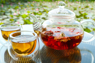 Closeup of a pot of rose tea with two cups of tea on garden table