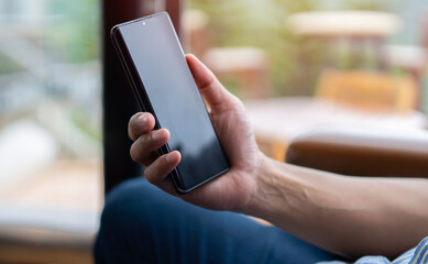 Cropped image of men's hand holding mobile phone on sofa at home office.