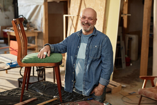 Waist up portrait of smiling senior craftsman looking at camera in furniture restoration workshop, copy space