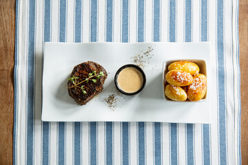 Appetizing medium rare grilled beef steak with baked potato and sauce served on white plate.