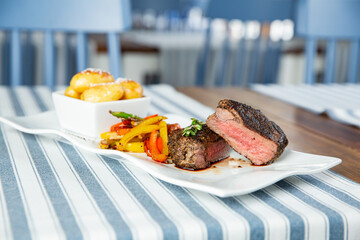 Appetizing medium rare grilled beef steak with baked vegetables served on white plate.