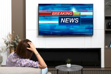 Back view on excited man sitting on the couch and watching breaking news on tv at home	