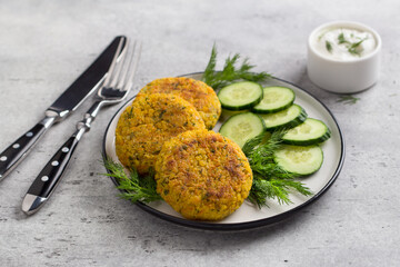Delicious millet cutlets with carrots and seeds served with cucumber and herbs on a gray textured background, top view. Homemade vegan food - 642024632