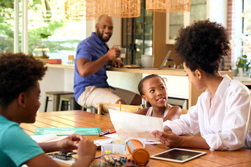 Family Around Table At Home Using Laptop With Parents Helping Children With Science Homework