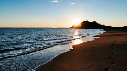 遠くの岬に沈む長い砂浜の夕日