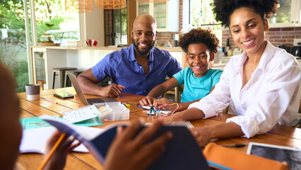 Family Around Table At Home Using Laptop With Parents Helping Children With Science Homework