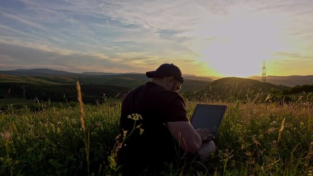 Active and mobile man with laptop sitting in a chair, in the contryside and networking