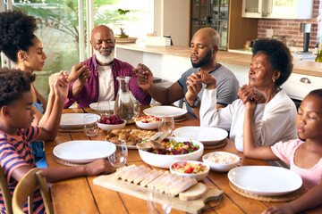 Multi-Generation Family Joining Hands And Saying Prayer Before Meal At Home 