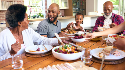 Multi-Generation Family Sitting Around Table Serving Food For Meal At Home Together