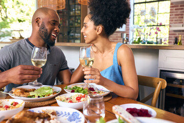 Couple Sitting Around Table At Home Doing Cheers With Wine Before Meal