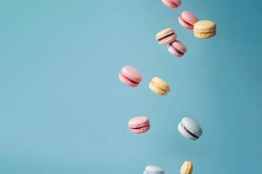 Colorful French macarons falling on the pastel blue background. Creative sweet food design concept.